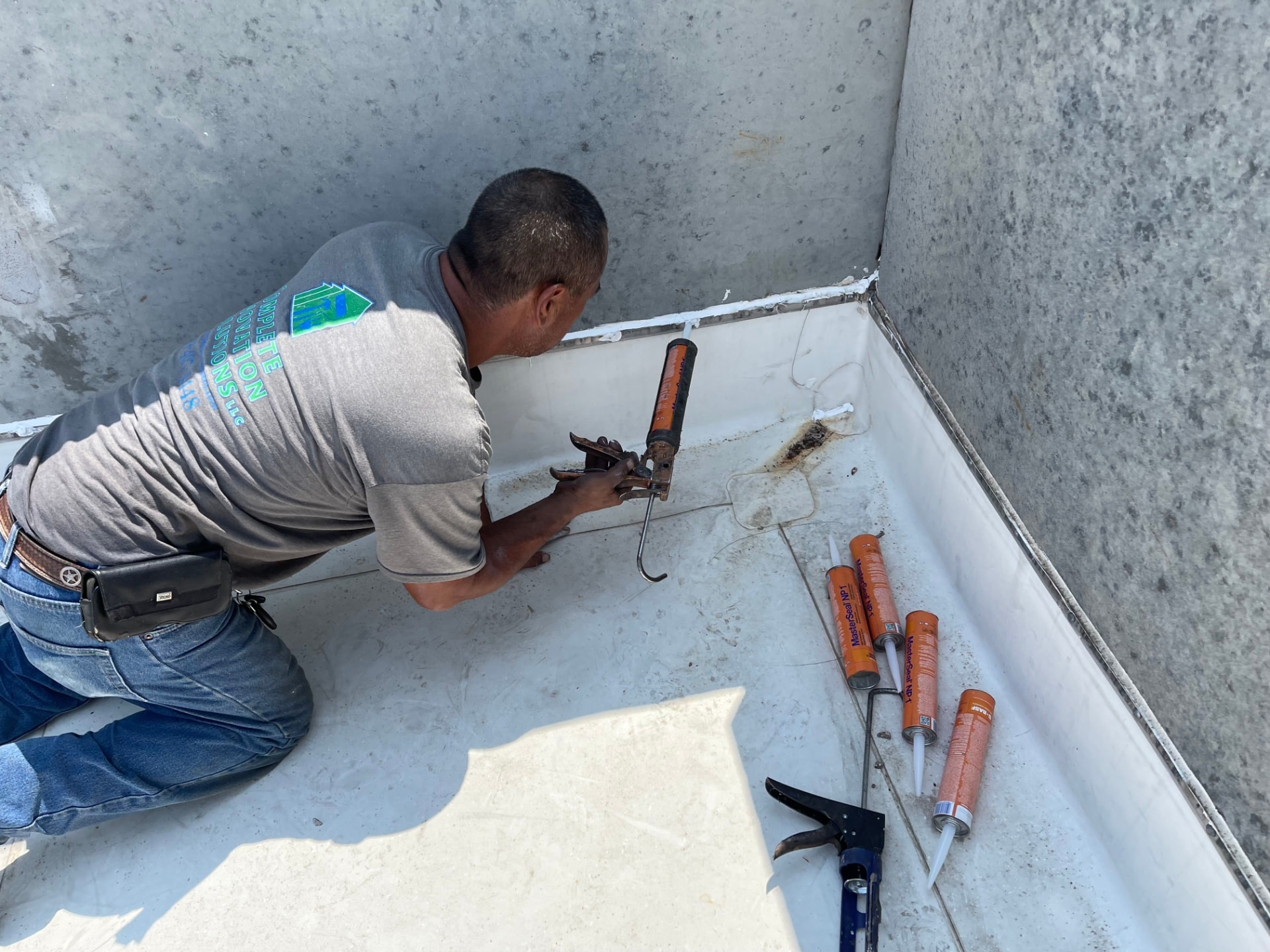 Commercial roofer running a bead of MasterSeal NP1 sealant along the top edge of a membrane termination at a parapet wall
