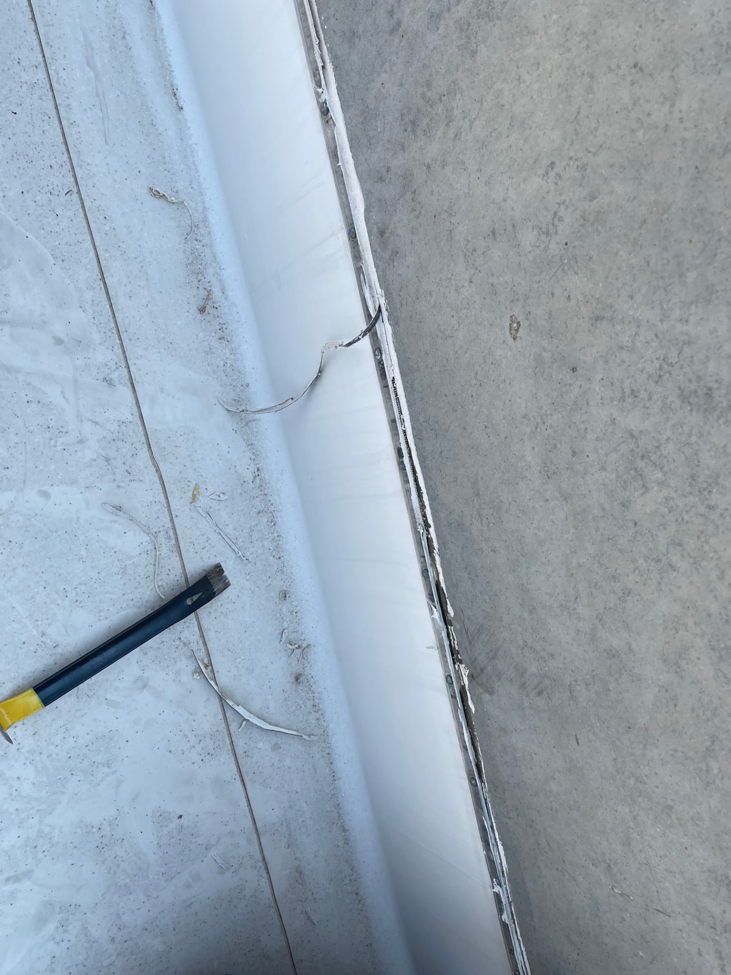 Close-up of a single-ply membrane termination bar and fastener line sealed against a concrete parapet wall on a commercial roof
