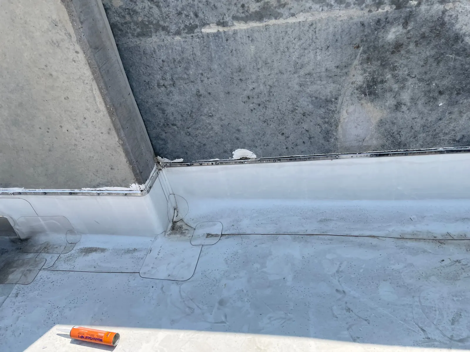 Inside corner of a commercial membrane roof showing target patches at the parapet transition and a sealed counterflashing line