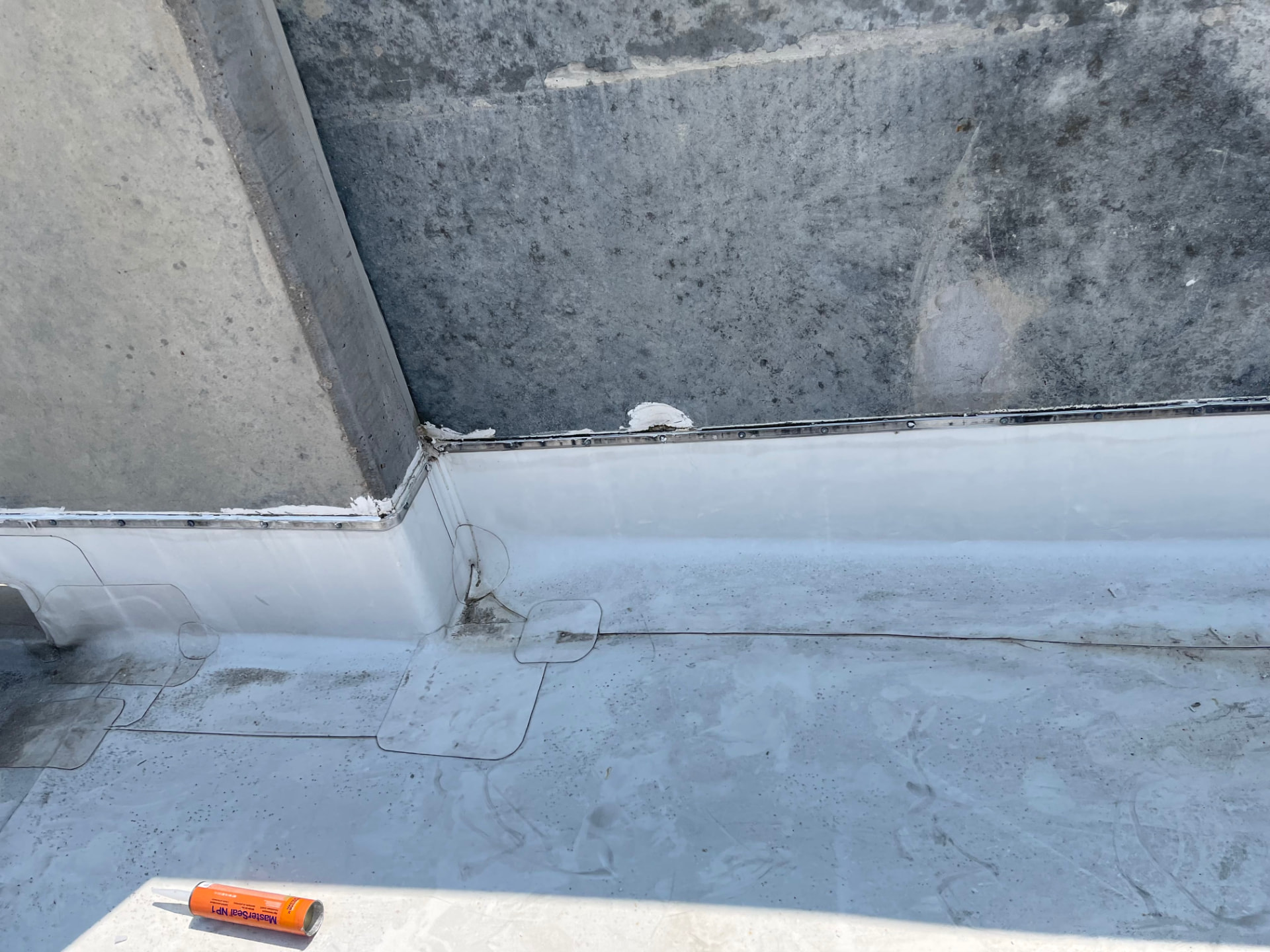 Inside corner of a commercial membrane roof showing target patches at the parapet transition and a sealed counterflashing line