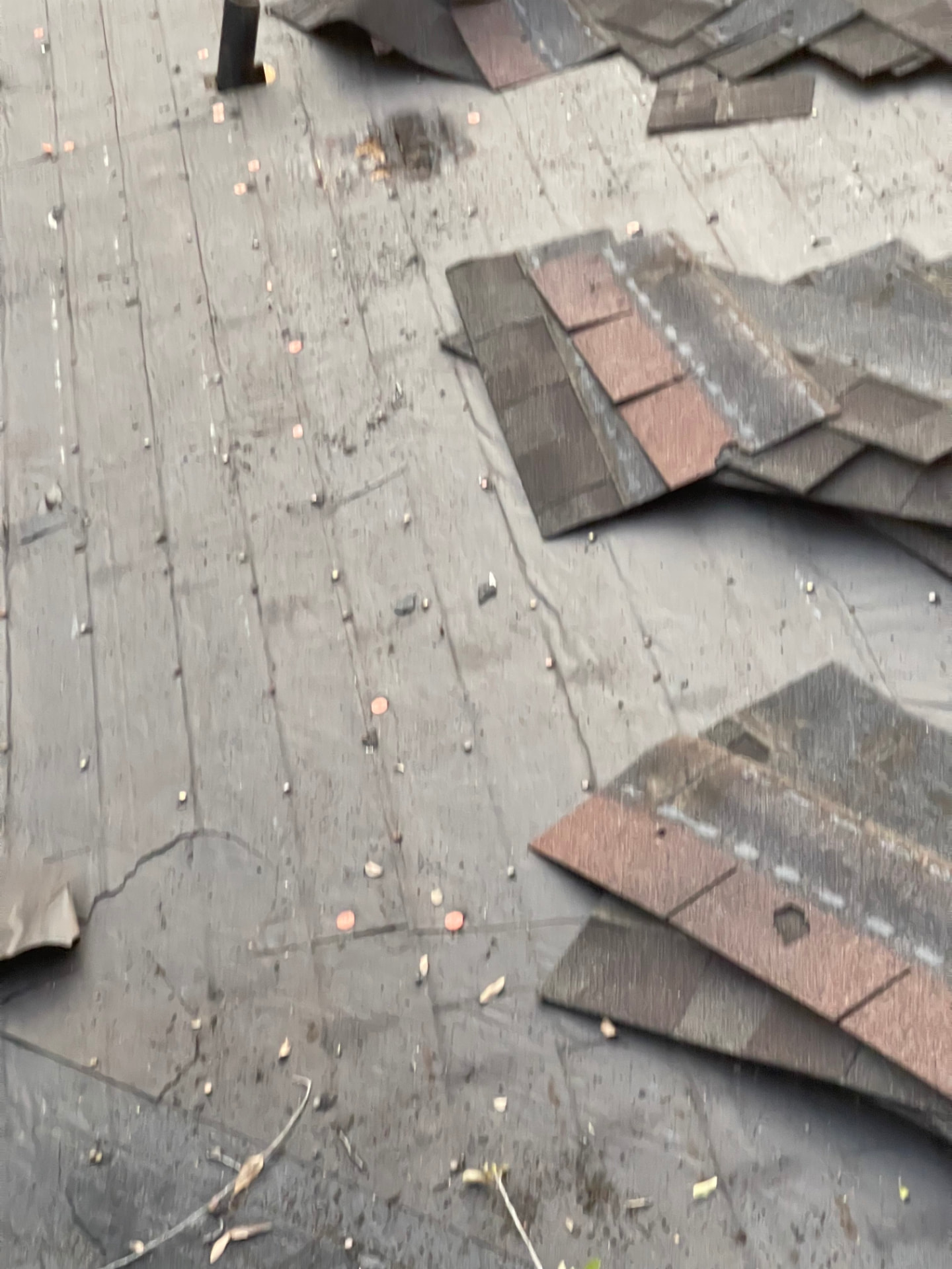 Roof deck exposed during tear-off with loose nails scattered across the underlayment and stacked bundles of removed shingles