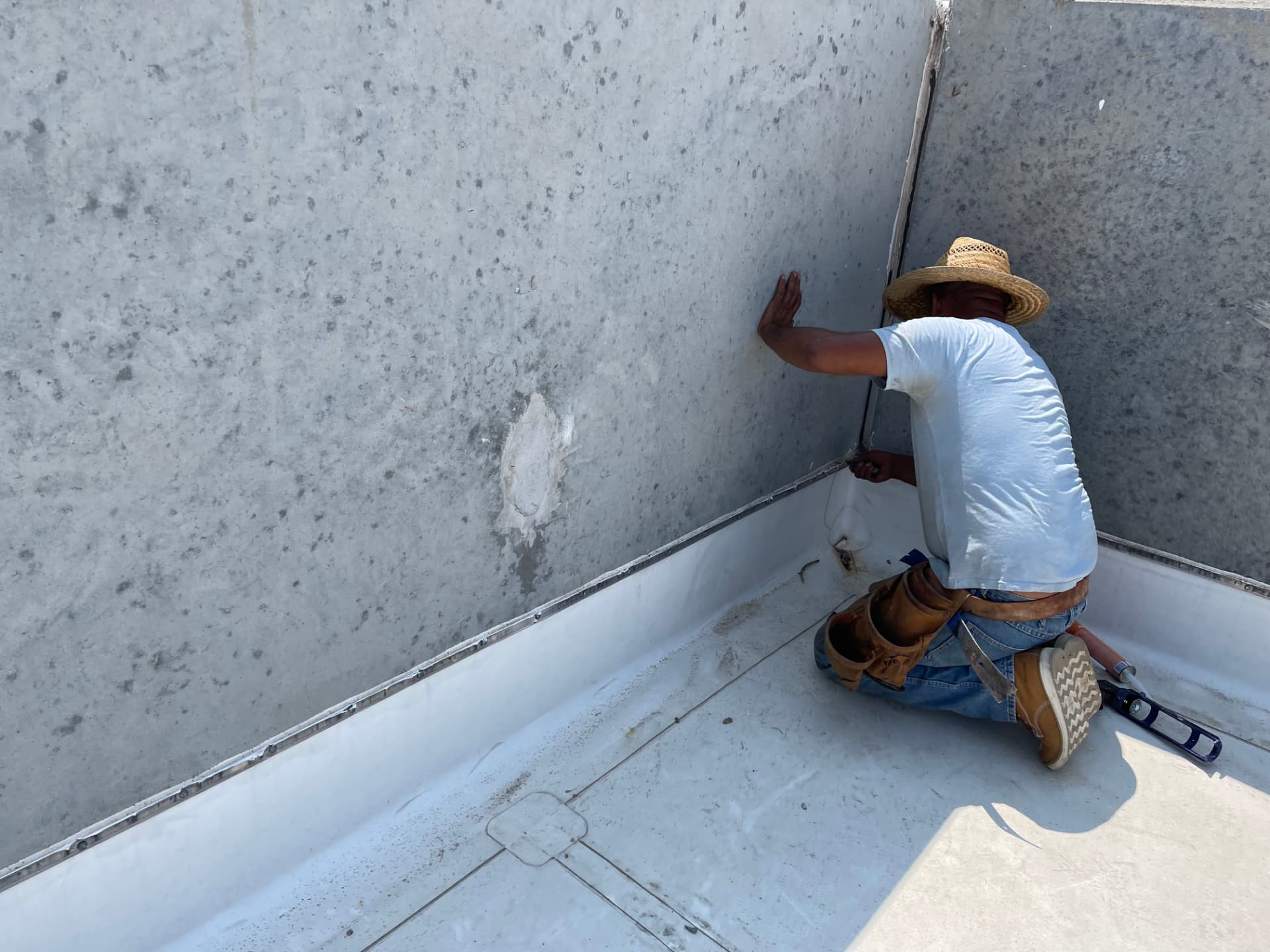 Homebase Roofing crew member kneeling at a concrete parapet wall detailing the membrane termination on a commercial low-slope roof
