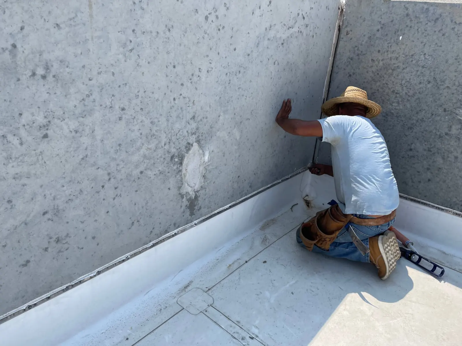 Homebase Roofing crew member kneeling at a concrete parapet wall detailing the membrane termination on a commercial low-slope roof
