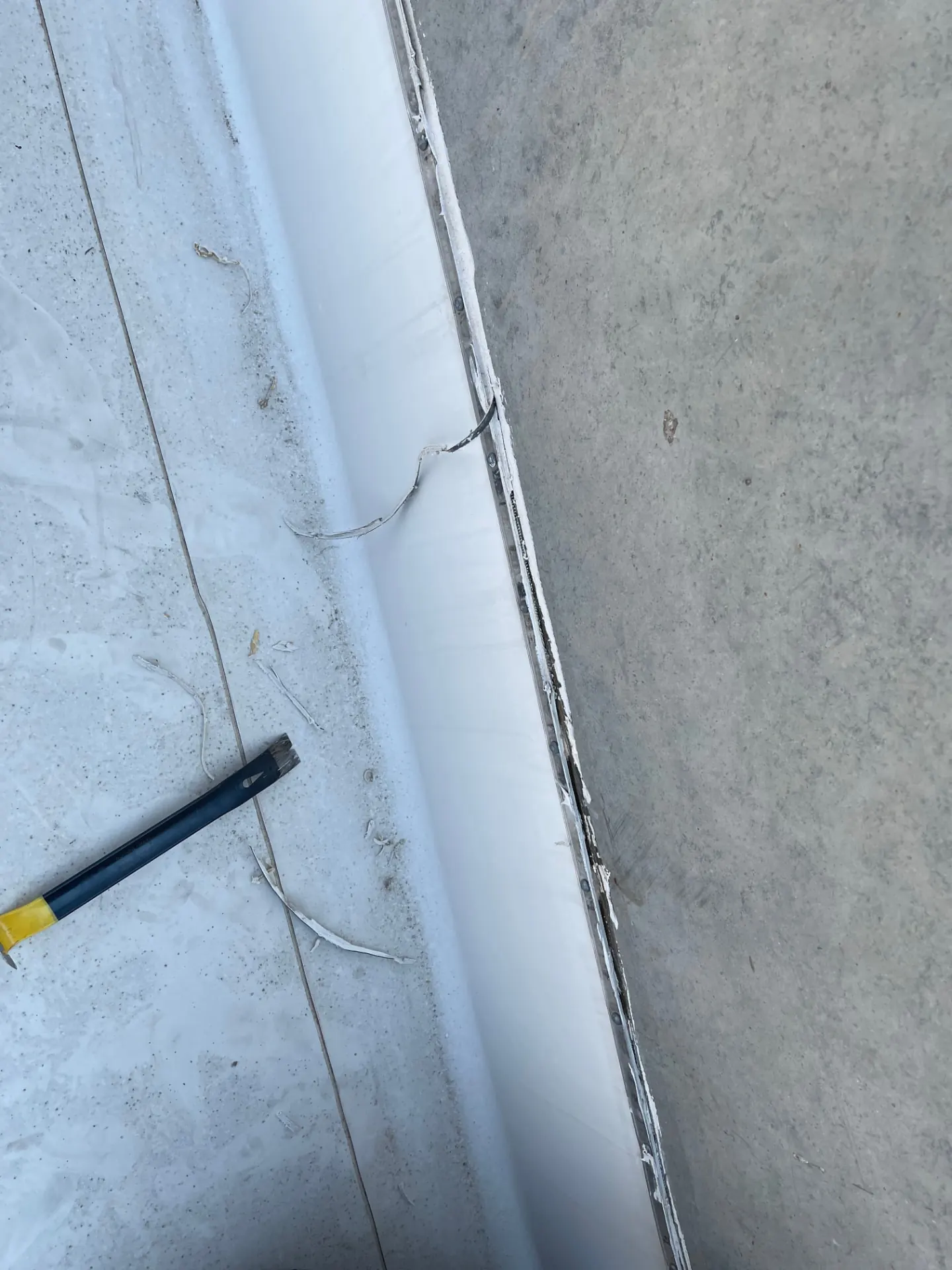Close-up of a single-ply membrane termination bar and fastener line sealed against a concrete parapet wall on a commercial roof
